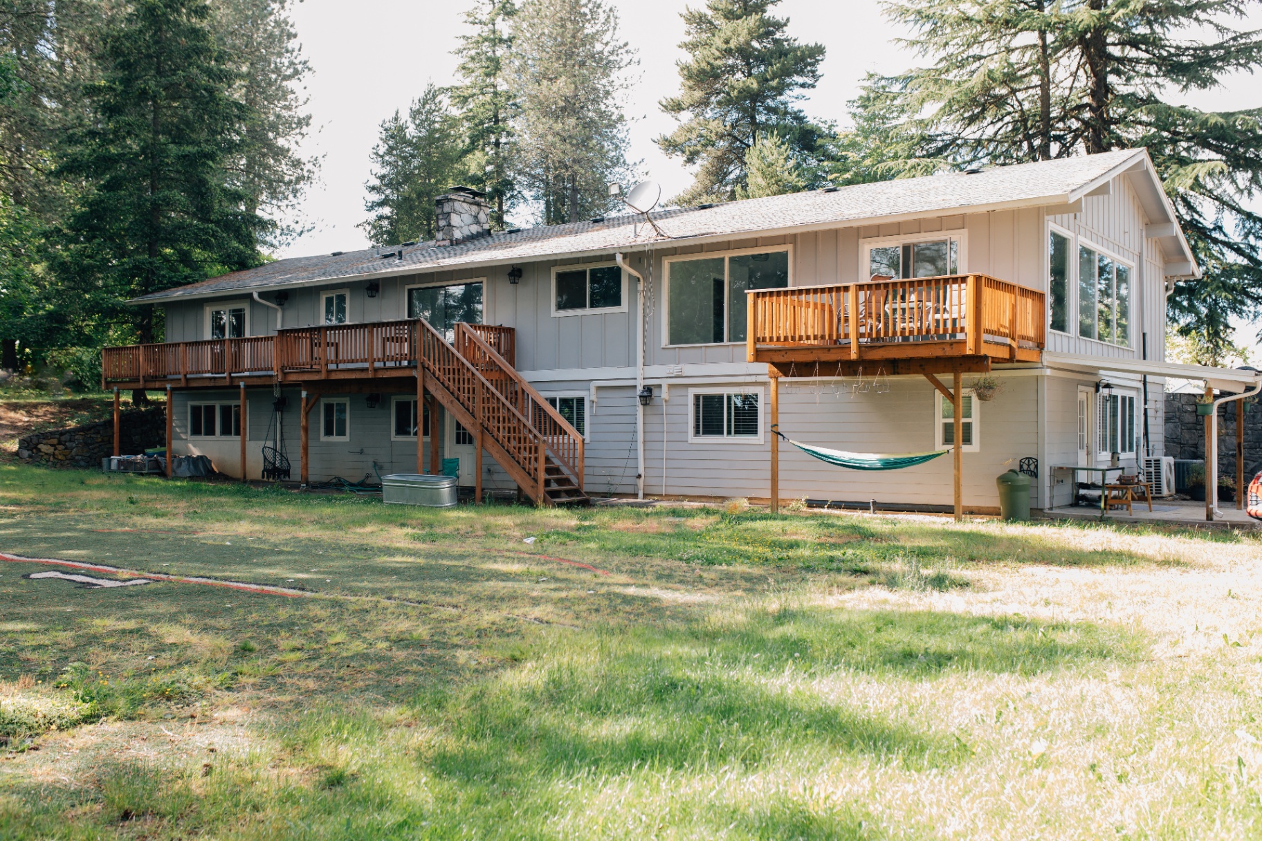 Back of the house with two decks, lawn, and tall evergreens
