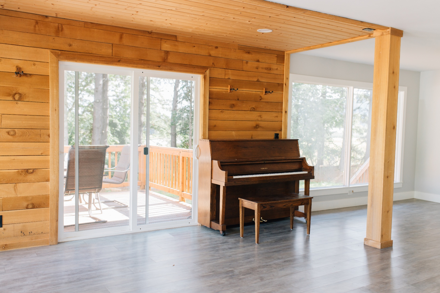 Open room with cedar walls, sliding door to deck, and an upright piano
